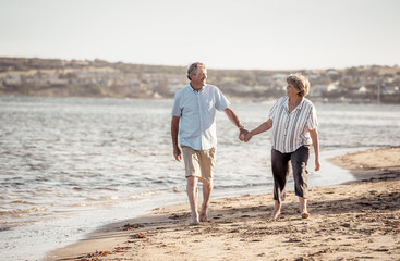Healthy active senior couple holding hands, embracing each other and walking on beach