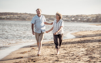 Healthy active senior couple holding hands, embracing each other and walking on beach