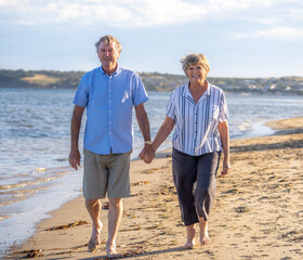 Healthy active senior couple holding hands, embracing each other and walking on beach