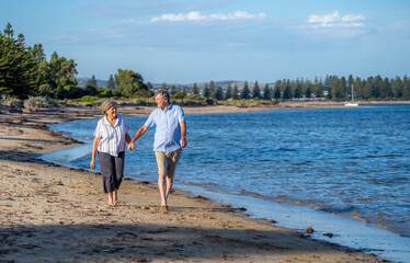 Healthy active senior couple holding hands, embracing each other and walking on beach