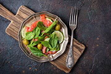 Tasty green salad with salmon, fresh spinach, olives, lime and cucumbers