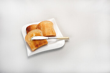 Three slices of toast on white plate.  White surface. Knife with butter.