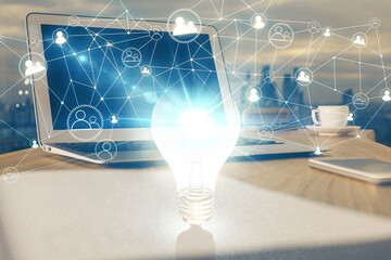 Computer on desktop in office with bulb icon hologram. Multi exposure. Concept of idea.