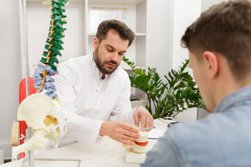 Doctor showing flexible spine model to his patient and explains the cause of his pain in medical office. Patient visiting physiotherapist in clinic. Surgery, healthcare and medicine concept.