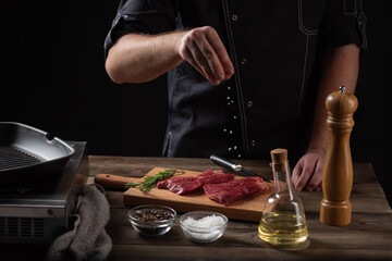 the chef sprinkles salt on the raw beef steak