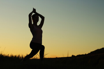 Silhouette of young woman doing yoga outdoors  Beautiful evening sunset  Sport activities health and wellness concept Space for text