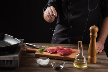 the chef sprinkles salt on the raw beef steak