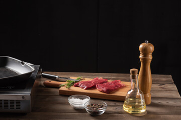 raw beef steaks on wooden board with ingredients, black background