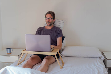 Caucasian young man working from home. Laptop on his bed. Home office.