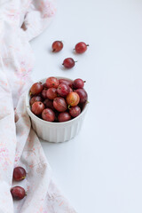 Ripe sweet gooseberry berries in a white bowl on a white table. Vertical photo