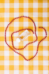 Composition of perfume bottle and bead necklace. Top view flat lay. Checkered yellow background.