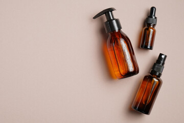 Set of amber glass cosmetic bottles on brown background. Pump bottle, dropper bottle, dispenser cosmetic container Flat lay, top view.