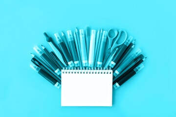 Back to school background with opened notepad and variety of school supplies in trendy aqua color. Flat lay. Close-up. Copy space. Mockup for your design.