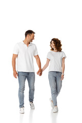 happy woman and cheerful man holding hands and looking at each other while walking on white