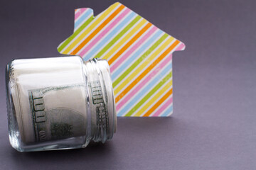 Real estate and property concept. Striped house cut out of paper and rolled money on grey background.