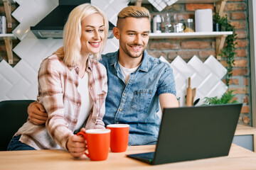 Happy couple drink coffee and using laptop relax together at their kitchen