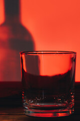 Empty transparent glass and shadow of bottle on the wall. Red lighting in the bar. Small clean glass on table.