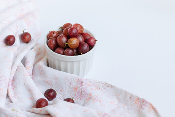 Ripe sweet gooseberry berries in a white bowl on a white table.