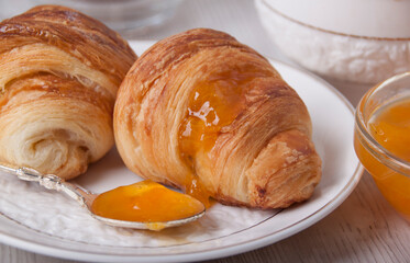 On a white plate is a croissant  with apricot jam