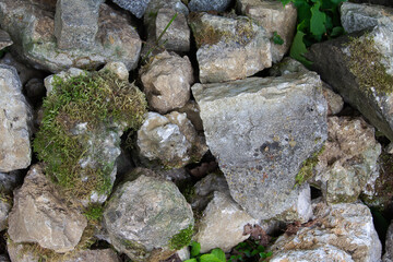 Texture natural stone wall overgrown with moss. Large and small stones form the wall.
