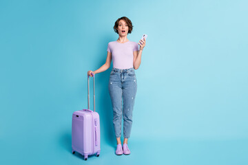 Full body photo of astonished girl tourist hold luggage use cellphone impressed quarantine border taxi hotel close wear lilac violet denim jeans isolated blue color background