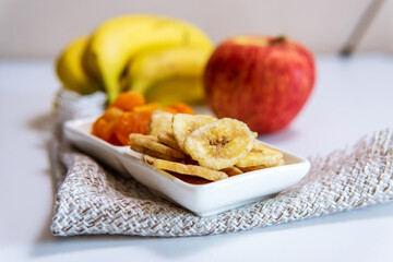 bowl of dried organic banana chips with fresh bananas, dried apricots, Apple. snack