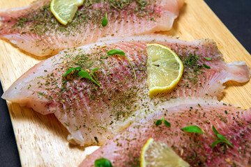 Tilapia with lemon and spices on cutting board. St. Peters fish.