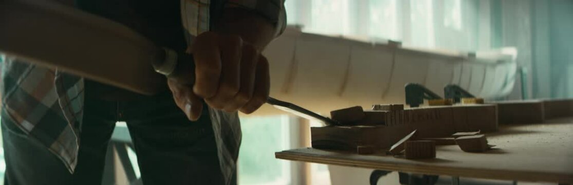 CU Caucasian male shaping canoe paddle with a chisel in his workshop. Boat making hobby, small business owner. Shot on RED Dragon