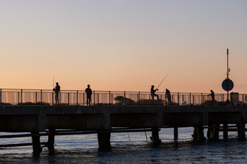 fishermen fishing with fishing rods on a pier at sunrise