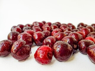 Scattered red cherry on a white background with drops of water.