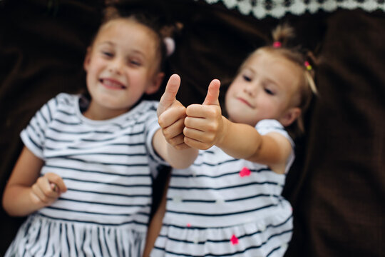 Two happy girls lying on a brown blanket and showing thub up. Top view