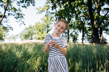 Girl in a striped dress with a flower in his hands looks at the camera. Happy summer