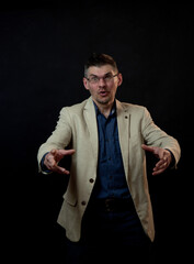 speaking actor in glasses wearing beige suit poses with hands ahead standing against black studio...
