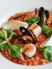 Seafood risotto. Risotto in tomato sauce with mussels, salmon, squid and shrimp. Garnished with lettuce. Traditional italian food. Dinner at an Italian restaurant.