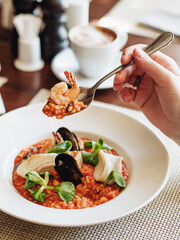 Seafood risotto. Risotto in tomato sauce with mussels, salmon, squid. A screech is visible on a raised spoon. Garnished with lettuce. Traditional italian food. Dinner at an Italian restaurant.