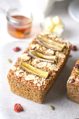 Loaf of Vegan Oatmeal Banana Bread topped with nut, seed, almond slide and banana set on cafe table.
