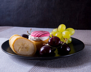A black plate with cherries, grapes, a banana, a cupcake lies on a table and a bunch of flowers in the background