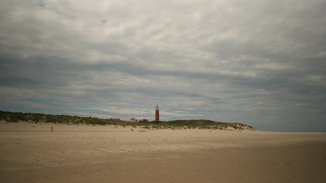 Wide, empty beach with lighthouse and person walking the dog on Texel island, Netherlands.