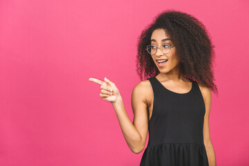 Portrait of a happy young african american woman pointing fingers away at copy space isolated over pink background.