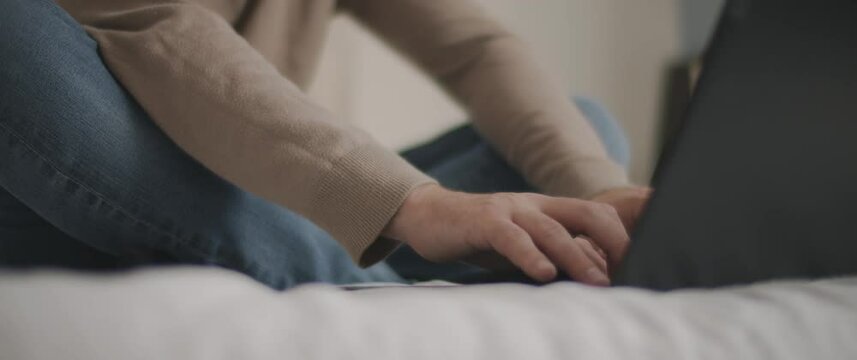 Man hands typing something on a laptop keyboard in the bedroom. Slow motion, shallow depth of field, BMPCC 4K