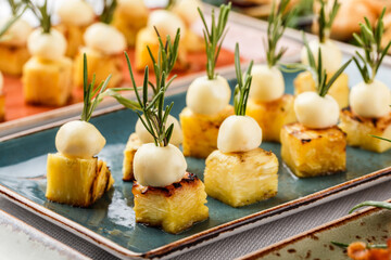 Delicious appetizers with cheese and pineapple in plate on banquet table. Catering food, canape and snacks, close up