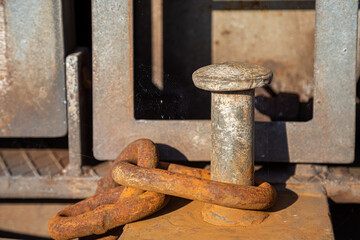 Eine starke, verrostete Kette hängt an einem Poller im Hafen