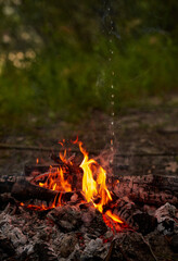 Burning wood at night. Bonfire in a tourist camp in nature in the mountains. Flames and fire sparks on a dark abstract background. Outdoor barbecue. The infernal element of fire. Fuel, power and energ