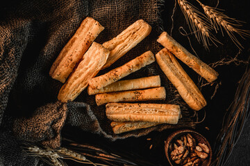 Puff bread sticks with sesame on rustic sackcloth background with wheat spikelets. Pastries and bakery, top view