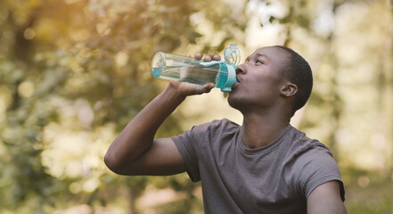 Young black man drinking water from sport bottle at park