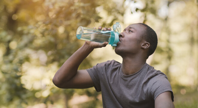Young Black Man Drinking Water From Sport Bottle At Park