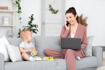 Woman talking on cellphone and using laptop while looking after toddler son