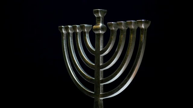 A silver menorah spins and glimmers in the soft warm light with a black background.