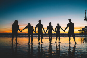 Fototapeta na wymiar People's silhouette holding hands enjoying friendship and trip to tropical island during summer vacations, group of friends having fun on seashore at sunset. Happiness, success, friendship, community