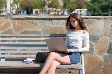 woman sitting on a bench in the park and working on a laptop